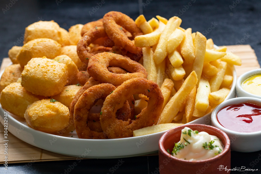 Porção mista frita em prato branco redondo com molhos, Mixed portion with fritras, cassava and onion Porção mista frita em prato branco redondo com molhos, Mixed portion with fritras, cassava and onion
