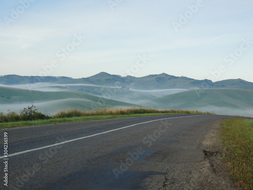 Empty Road and landscape. Mist at asphalt. Fog at highway. Nature in countryside with green hills. Travel and journey. Route in summer. Freeway view with background. Horizon perspective. Outdoor.