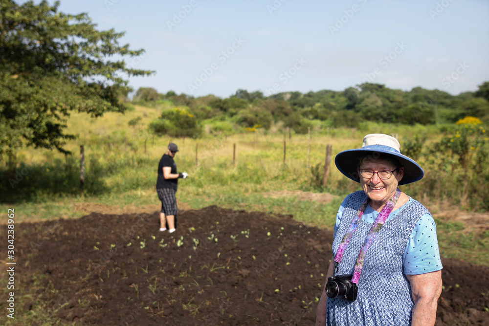 Grandmother smiling at camera while grandson works in community garden while volunteering in South Africa
