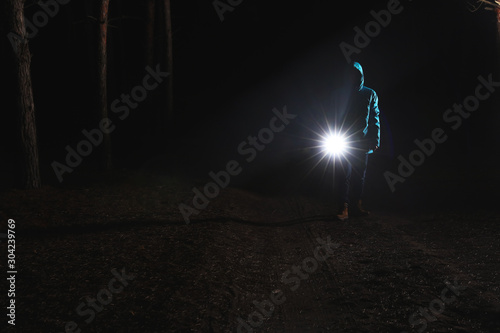 Man with bright flashlight in forest at night