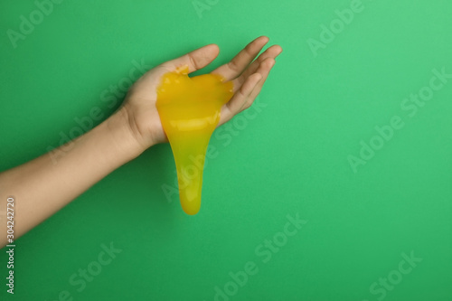 Woman playing with yellow slime on green background, closeup. Antistress toy