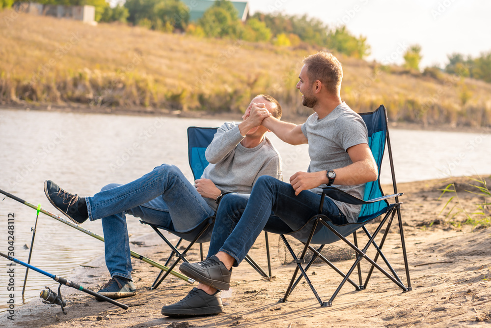 leisure and people concept. Happy friends with fishing rods on pier by lakeside. leisure and people concept. Happy friends with fishing rods on pier by lakeside.