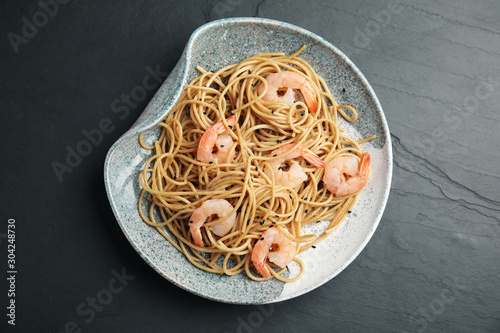 Plate of tasty buckwheat noodles with shrimps on black table, top view