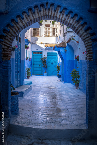 Portrait view of the city and doorway. Traditional house in the background. Sunny day in blue city Chefchaouen, Morocco. © The Walker