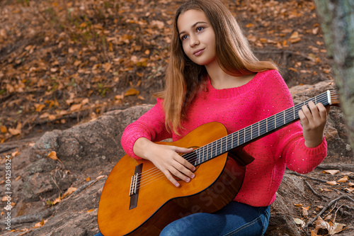 Teenage girl plays guitar outdoors in autumn
