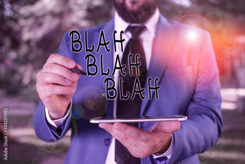 Writing note showing Blah Blah Blah. Business concept for Talking too much false information gossips nonsense speaking Businessman in blue suite stands with mobile phone in hands photo