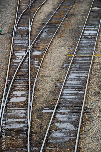 Looking down on the train tracks in a railroad yard. May rows of train tracks and a switch are visible.