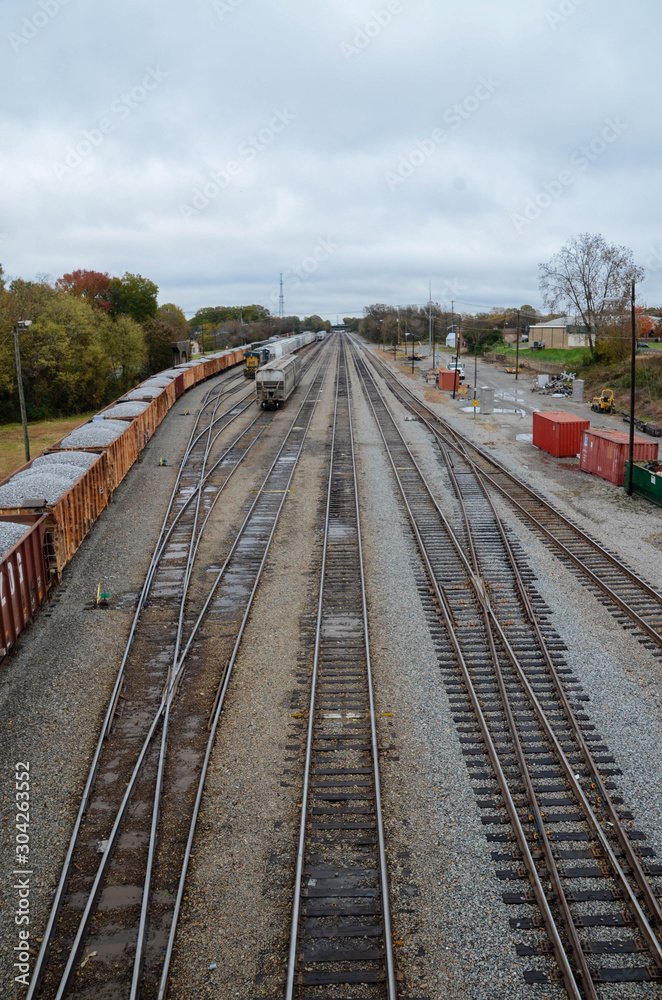 Obraz premium Looking down on a railroad train yard. Lots of railroad switches in view. Loaded car with gravel on one line. Locomotive and other cars are visible.