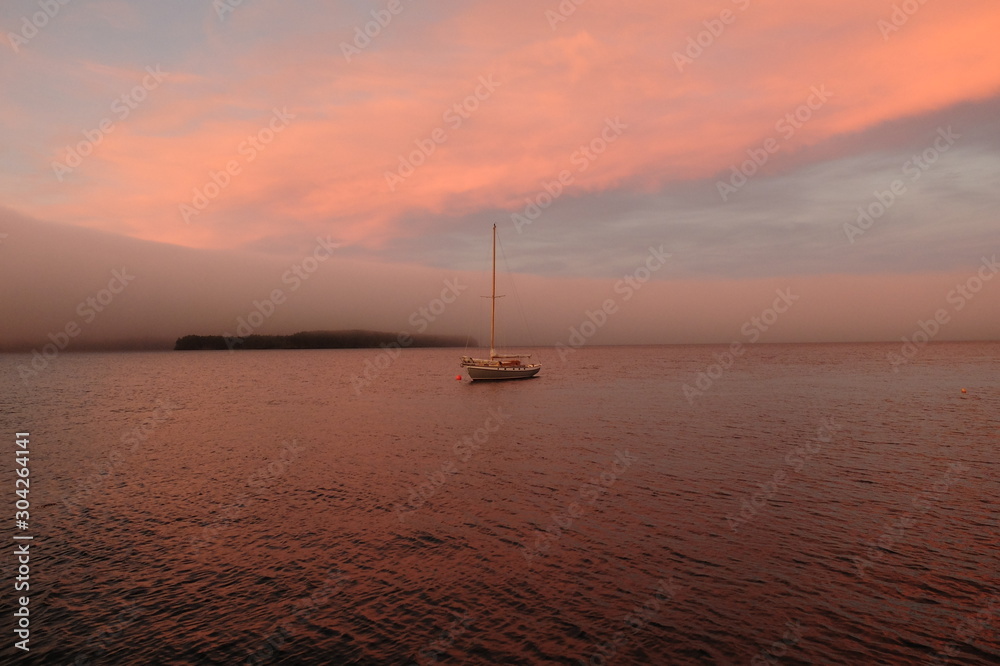 Sailboat moored at sunset near a fog bank.