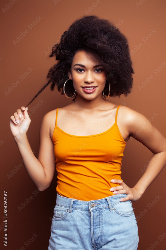 pretty young african american woman with curly hair posing cheerful gesturing on brown background, lifestyle people concept pretty young african american woman with curly hair posing cheerful gesturing on brown background, lifestyle people concept