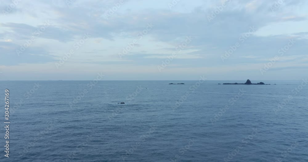 Aerial view passing above ocean water waves small tiny rock islands offshore against horizon skyline. Aerial view passing above ocean water waves small tiny rock islands offshore against horizon skyline.