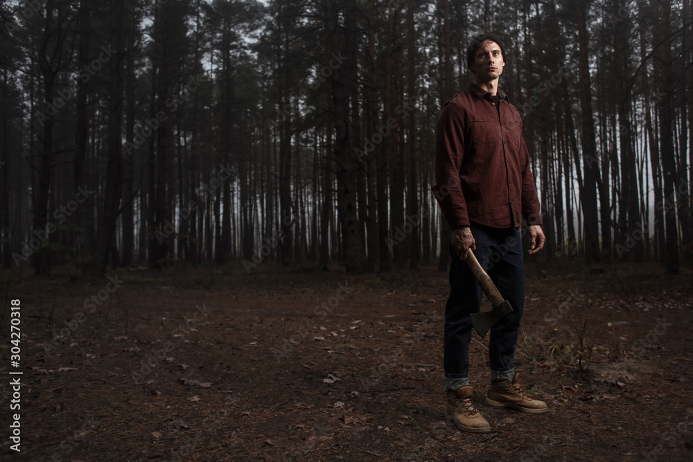 Strong lumberjack with the ax in the forest.Stylish lumberman getting ready for work. Lifestyle. Strong lumberjack with the ax in the forest.Stylish lumberman getting ready for work. Lifestyle.