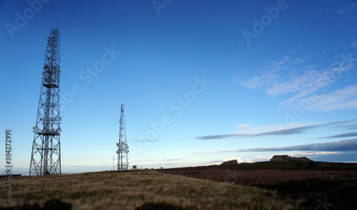 Slim silhouettes of telecommunication antennas in the evening sky.