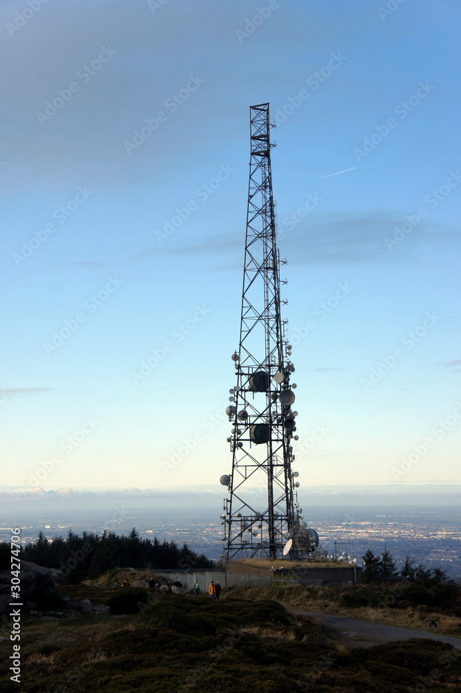 A thin silhouette of a telecommunication antenna in the evening sky.