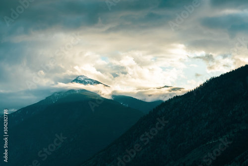 Snowcapped mountain peak surrounded by dramatic clouds and mist with sunlight