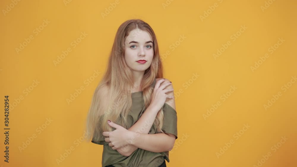 Smiling young woman in casual clothes holding hands crossed, isolated on orange wall background. People sincere emotions, lifestyle concept. Smiling young woman in casual clothes holding hands crossed, isolated on orange wall background. People sincere emotions, lifestyle concept.