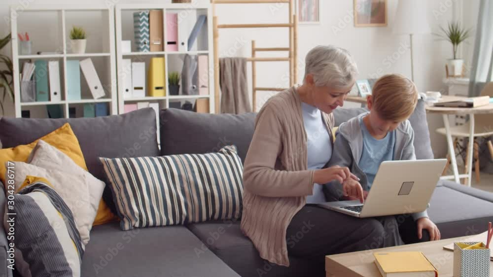 Lockdown of elderly attractive woman sitting on couch with her grandson and they using laptop together Lockdown of elderly attractive woman sitting on couch with her grandson and they using laptop together