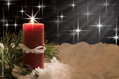 lit white candle and red ribbon with pine needles with beam of light in snow. Christmas Background with holiday theme. photo