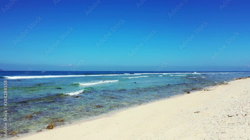 White waves splashing on rocky seashore of exotic beach with white sand on a bright blue sky background, copy space White waves splashing on rocky seashore of exotic beach with white sand on a bright blue sky background, copy space
