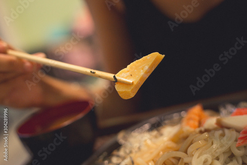 Closeup lady use chopstick to take sweet egg up for eating. Soba with sea food, cold noodle from Japan serve with crab and shimp meat eating with miso soup photo