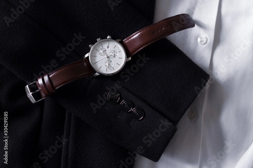 dark brown leather men's watches with white display with a black coat and white shirt as background