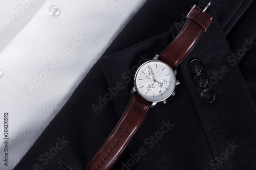 dark brown leather men's watches with white display with a black coat and white shirt as background