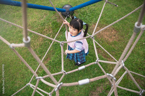 Little gile climbing the net. Happy kids on colorful ropes together in park. The girl on the playground. Little girl climbing in adventure park. photo