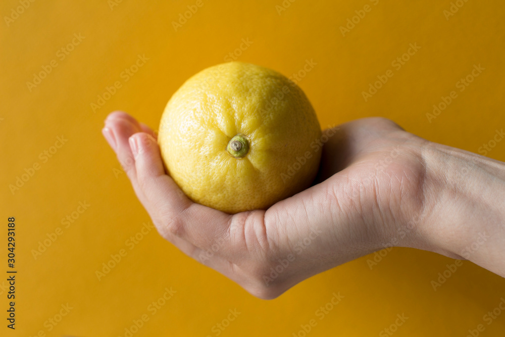 young woman holding a whole lemon on yellow background young woman holding a whole lemon on yellow background