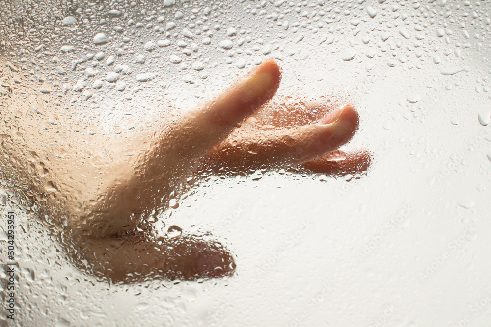 Fototapeta premium hand of a young woman behind glass with water drops on it reaching out