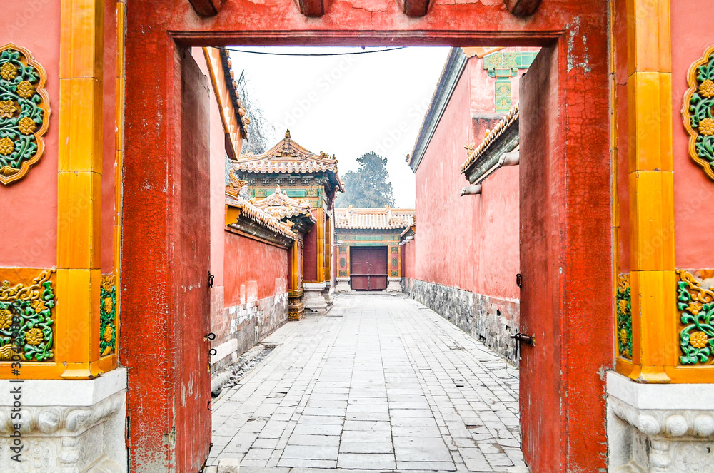 The gate door and red wall of Forbidden Palace with stone walking path between 2 buildings or house.