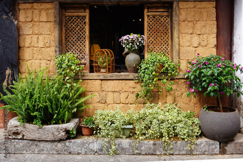 Fototapeta Naklejka Na Ścianę i Meble -  Fresh plants and flower outside a textured brick wall, with the intrigue bamboo window frame.  
