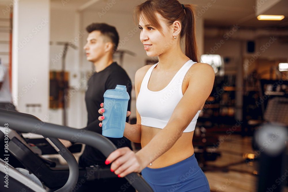 Couple in the gym. A woman performs exercises. Man in a black t-shirt Couple in the gym. A woman performs exercises. Man in a black t-shirt