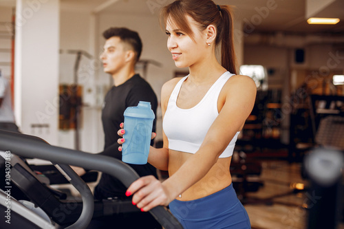 Couple in the gym. A woman performs exercises. Man in a black t-shirt