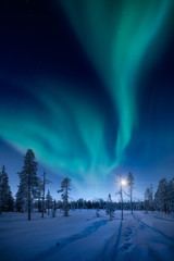 Moon and Northern Lights above Pallas fells with fresh snow at winter night in Pallas-Yllästunturi national park in Muonio, Finland
