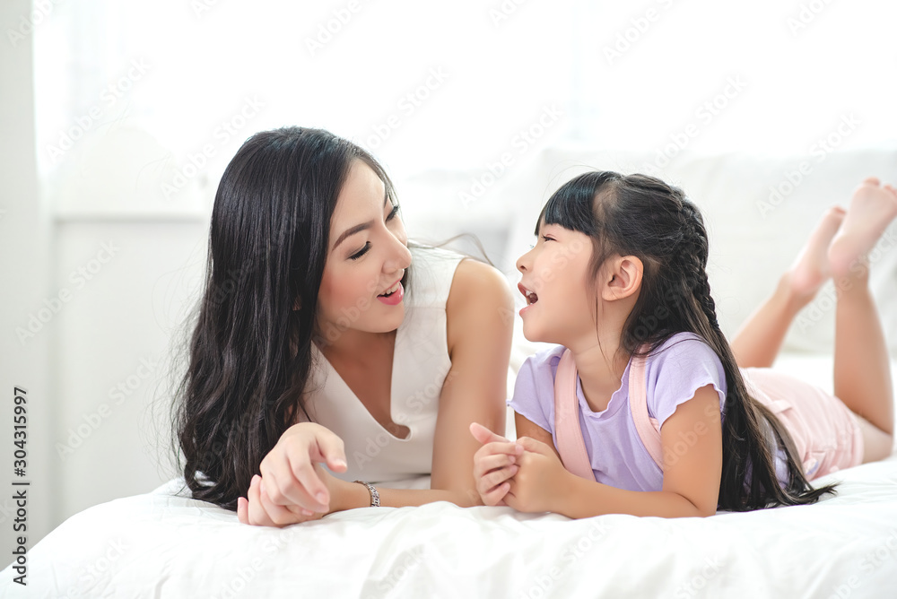 Mother playing with her daughter on the bed. The daughter is happy and laughing Mother playing with her daughter on the bed. The daughter is happy and laughing