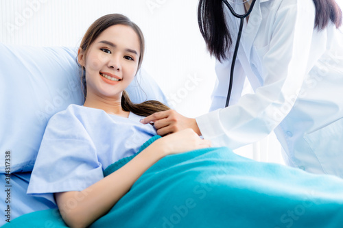 Asian young female patient on bed while doctor hands of checking examining his pulse for record the treatment results with smiley face very good symptom in hospital background.