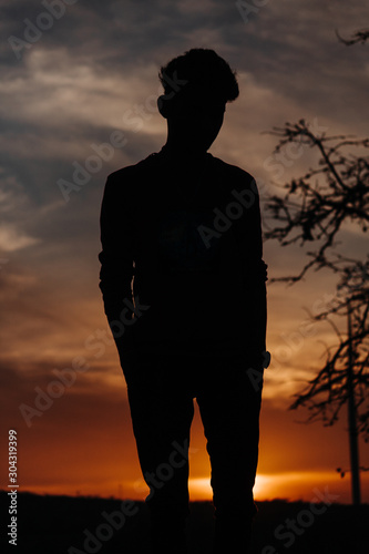 Silhouette of a man standing in front of trees and windmill during sunset