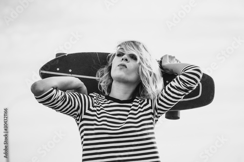 Urban stylish young sportive woman walking with skateboard. Close up portrait of a pretty young hipster girl chewing bubble gum.