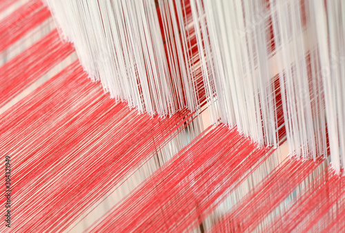 Close up of interlacing between white warp yarn and red weft yarn on traditional cotton weaving loom. Selective focus.