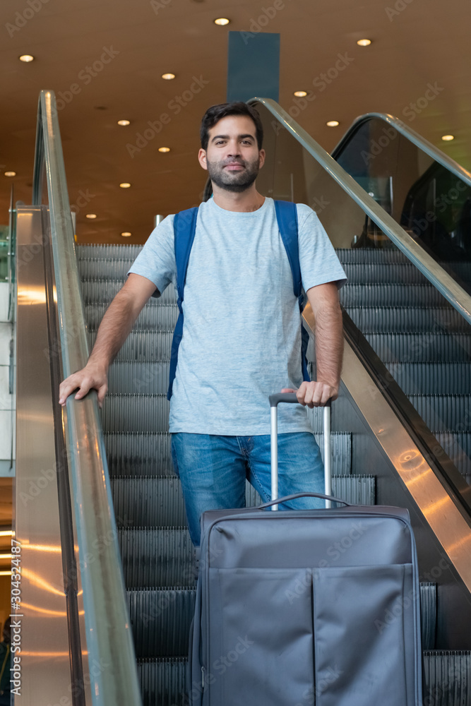 Cheerful traveler with suitcase on escalator. Cheerful traveler looking at camera. Travel concept