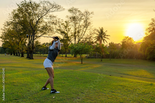 Healthy Sport. Asian Sporty woman golfer player doing golf swing tee off on the green course evening time, she presumably does exercise outdoor. Healthy Lifestyle Concept..