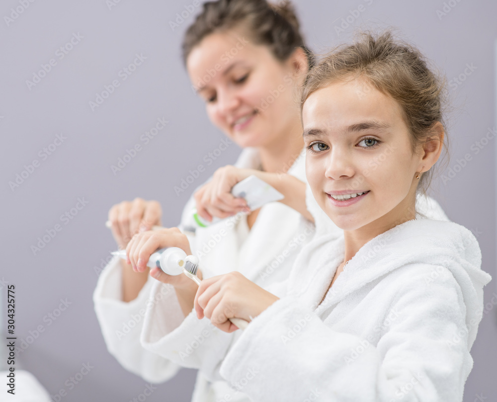 Happy family, mom and her daughter squeeze toothpaste onto toothbrushes in the bathroom at home Happy family, mom and her daughter squeeze toothpaste onto toothbrushes in the bathroom at home