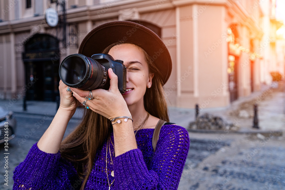 Casual stylish hipster traveler woman photographer in hat with a DSLR camera taking photos during traveling around european city