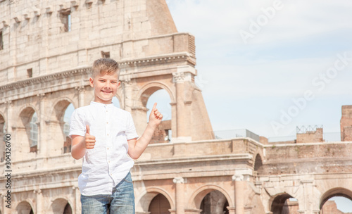 Happy boy shows thumbs up gesture at points on the coliseum in Rome, Italy. Travel concept. Empty space for text