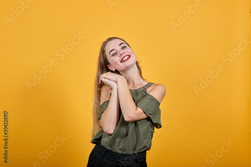 Young beautiful blonde woman wearing haki shirt looks happy and excited doing winner gesture keeping thumbs under chin. Celebration concept.