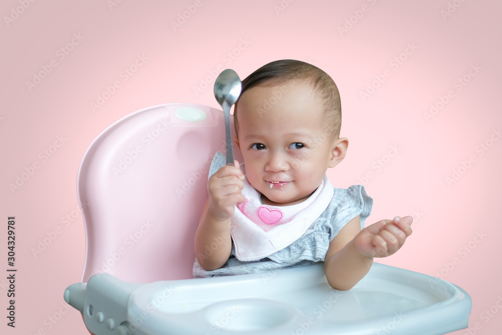 Cute little Asian 8 months old toddler baby girl eating healthy puree food isolated on pink background with clipping path, Self Feeding With Spoon, Encouraging Independence concept - Selective focus Cute little Asian 8 months old toddler baby girl eating healthy puree food isolated on pink background with clipping path, Self Feeding With Spoon, Encouraging Independence concept - Selective focus