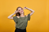Beautiful caucasian young funny woman wearing pretty shirt isolated orange background looking smiling and showing victory sign on eyes