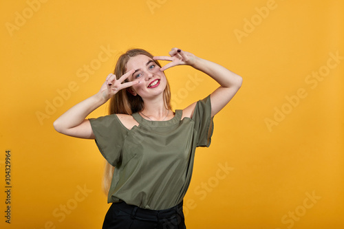 Beautiful caucasian young funny woman wearing pretty shirt isolated orange background looking smiling and showing victory sign on eyes © Petro