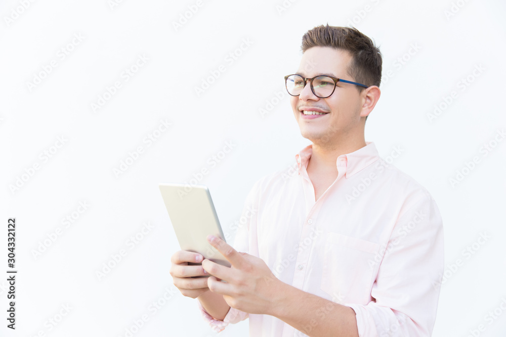 Pensive happy guy in eyeglasses holding tablet and looking at copy space away. Young man in glasses standing isolated over white background. Advertising concept Pensive happy guy in eyeglasses holding tablet and looking at copy space away. Young man in glasses standing isolated over white background. Advertising concept
