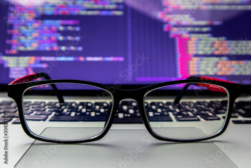 Glasses placed on the laptop At the back is the screen of the program source code. That programmers can develop into websites or mobile apps Which system analysts and designers have designed